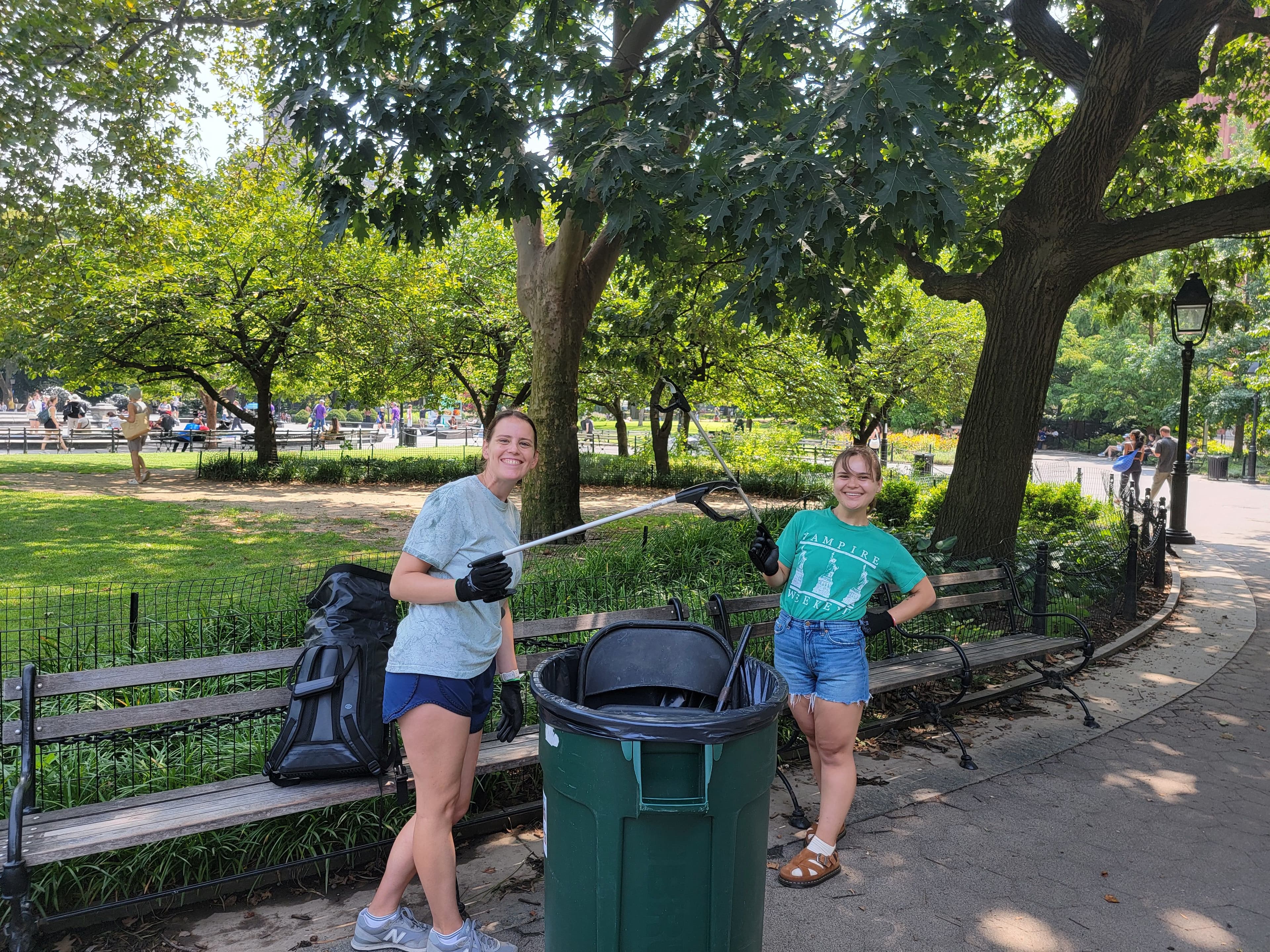 Two volunteers hold trash grabbers and stand around a garbage bin in Washington Square Park.