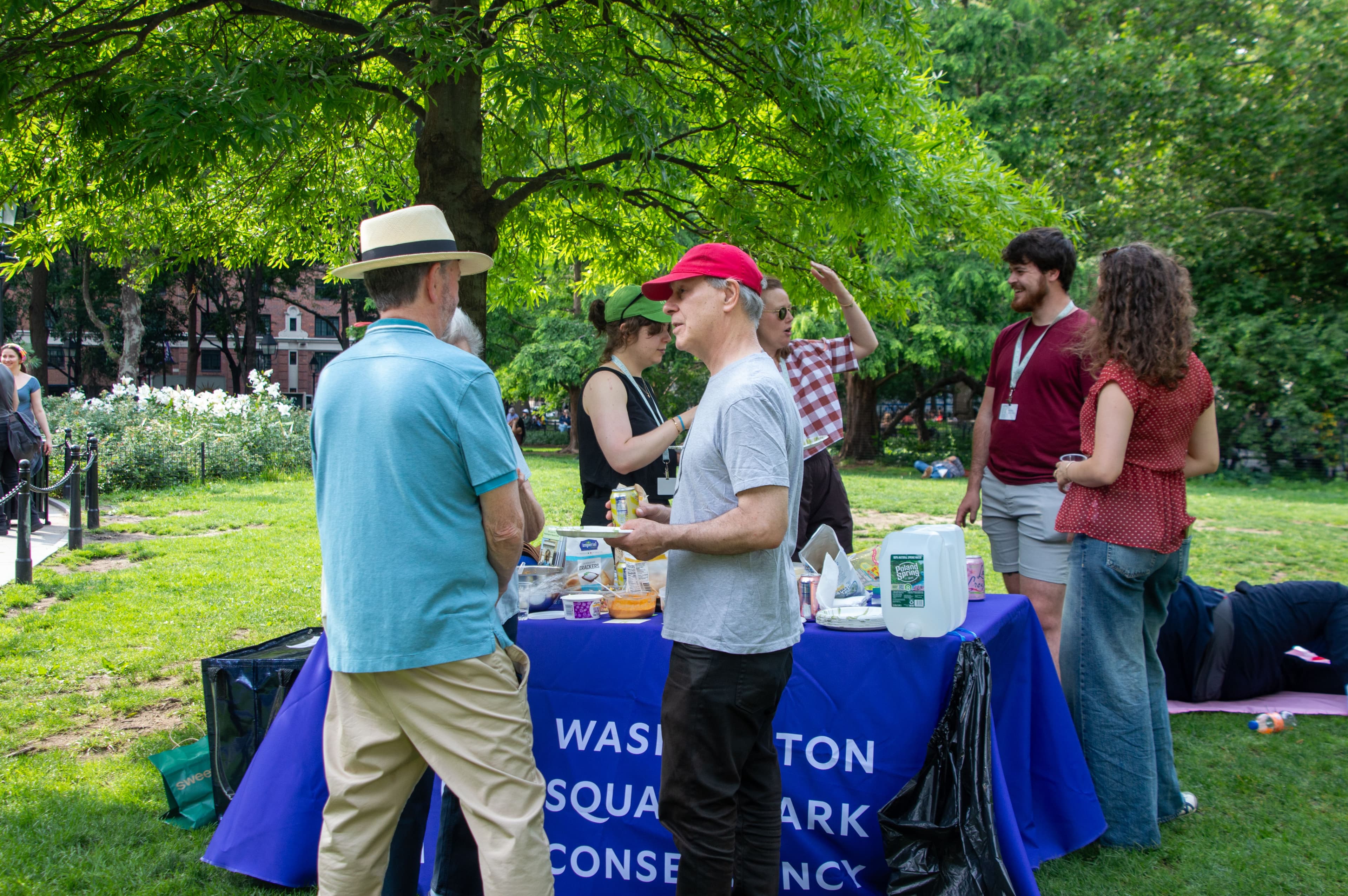 A small group of people has conversations around a Washington Square Park Conservancy table.